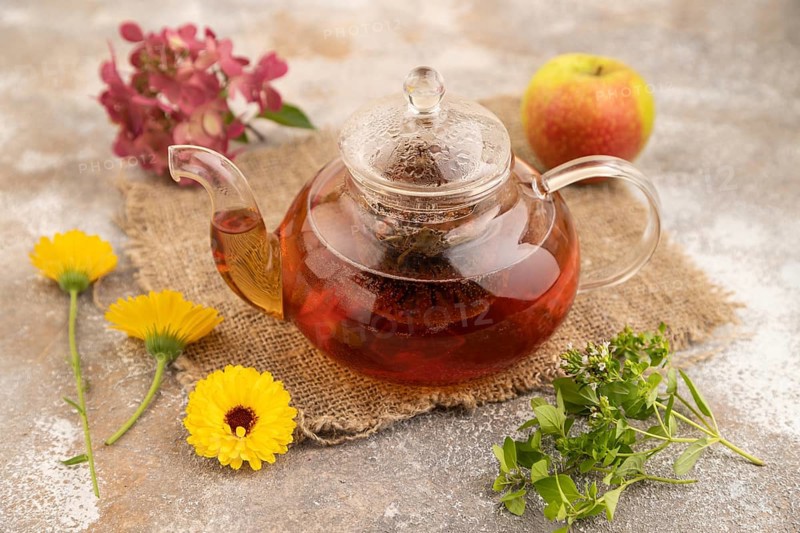 Red tea with herbs in glass teapot on brown concrete background and linen textile. Healthy drink concept. Side view, close up, selective focus