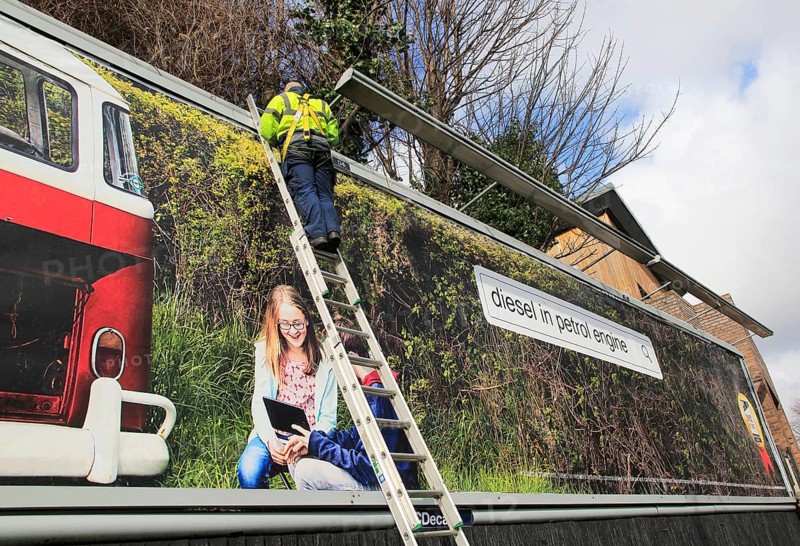 Man standing on ladder billboard for 'diesel in petrol engine' placed on advertising sign, city of Dublin, Ireland, Irish Republic Ireland, Europe