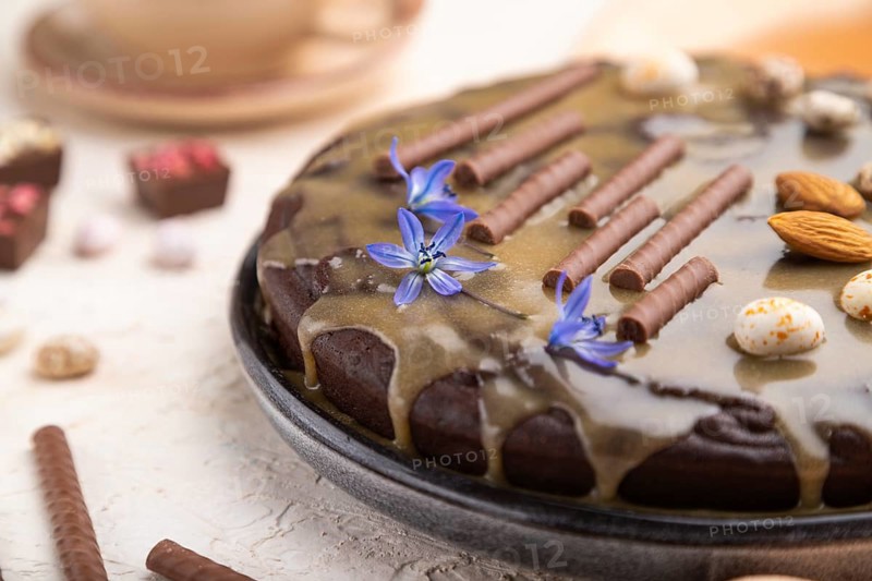 Homemade chocolate brownie cake with caramel cream and almonds with cup of coffee on a white concrete background and orange textile. Side view, close up, selective focus