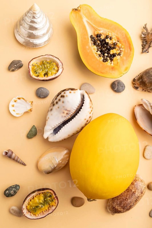 Ripe cut papaya, passion fruit, melon, seashells, pebbles on orange pastel background. Top view, close up. Tropical, healthy food, vacation, holidays concept