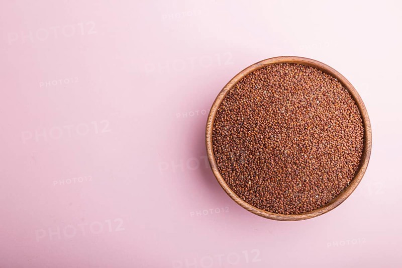 Wooden bowl with raw red quinoa seeds on a pastel pink background. Top view, flat lay, copy space