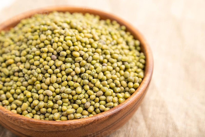 Wooden bowl with raw green mung bean on a white background and linen textile. Side view, close up, selective focus