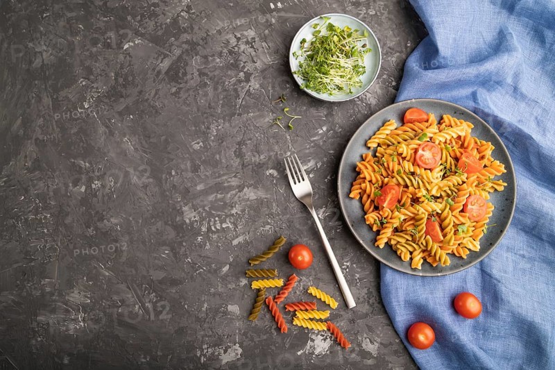 Tortiglioni semolina pasta with tomato and microgreen sprouts on a black concrete background and blue textile. Top view, flat lay, copy space