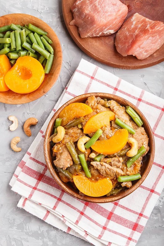 Fried pork with peaches, cashew and green beans on a black concrete background. top view, close up, flat lay, chinese cuisine. linen textile