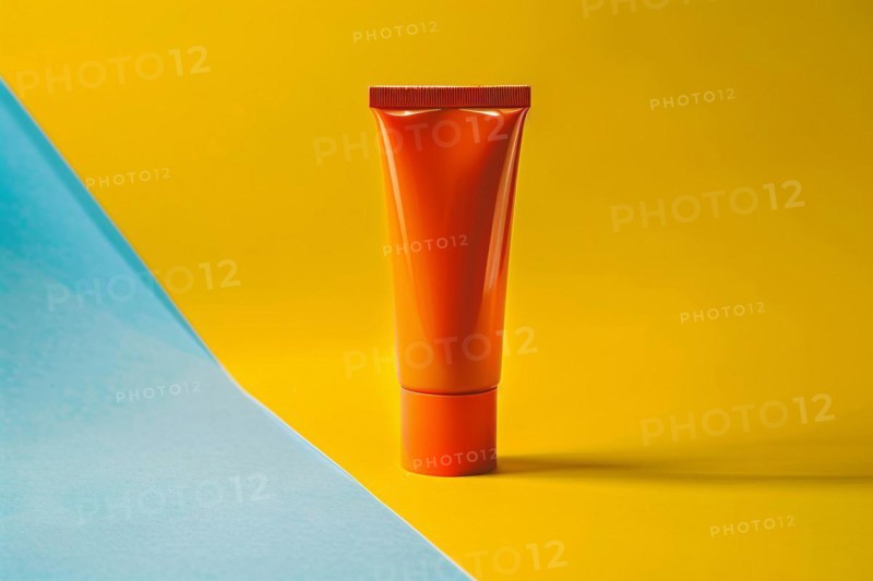 Orange sunscreen tube on yellow and blue studio background. KI generiert, generiert, AI generated