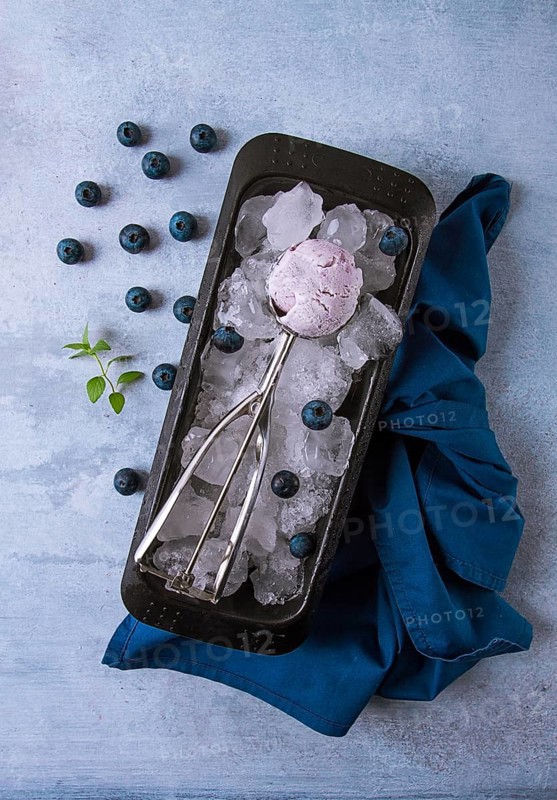 Blueberry ice cream, container with a spoon, on a gray table, fresh blueberries