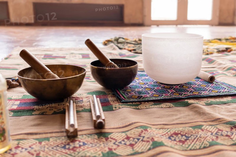 Instruments producing harmonic sounds, such as Tibetan and quartz singing bowls, placed on a blanket, prepared for a sound meditation, illuminated by bright light streaming in through a large window