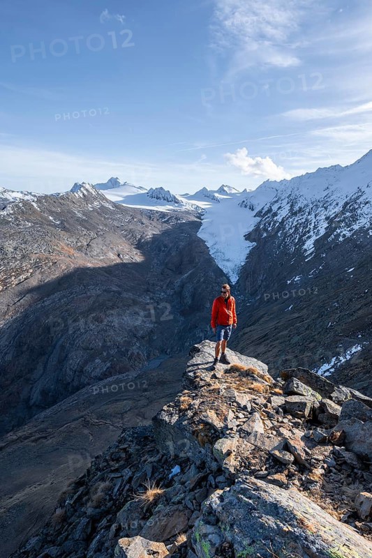 Mountaineer standing on a rock, surrounded by an impressive mountain landscape with snow-covered peaks in autumn View of Gurgler Ferner with summit Hochwilde and Falschungsspitze, Ötztal Alps, Tyrol, Austria, Europe