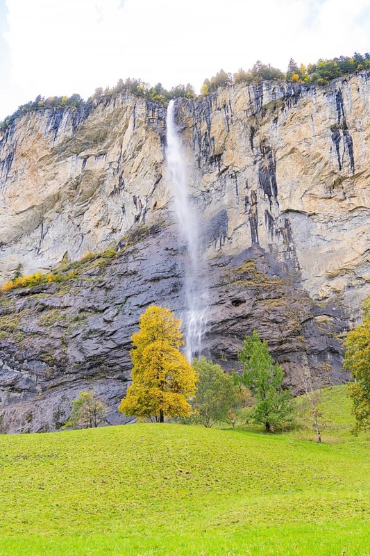 A waterfall flows down from high rocks, surrounded by trees in autumnal colours, Lauterbrunnen, Switzerland, Europe