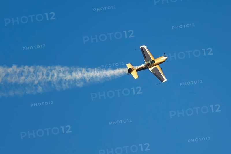 Golden stunt aerobatic plane performing stunts in blue sky with smoke trail. Concept of speed, difficulty, precision, risk