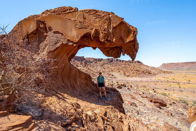 Young woman standing in a rock formation Lion's Mouth, Twyfelfontein, desert landscape, Kunene, Namibia, Africa