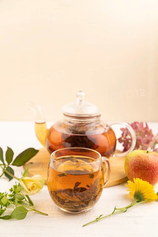 Red tea with herbs in glass teapot on white wooden background. Healthy drink concept. Top view, close up, selective focus