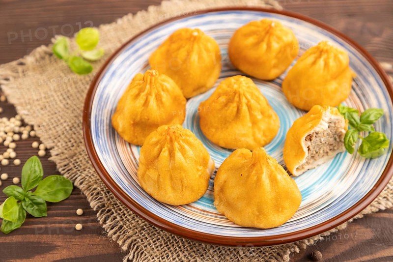 Fried manti dumplings with pepper, basil on brown wooden background and linen textile. Side view, close up, selective focus
