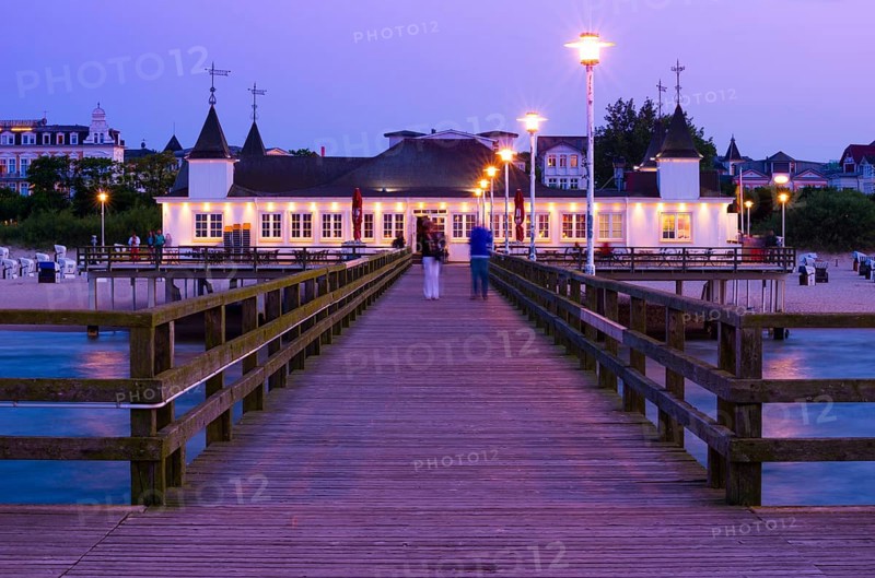 Illuminated pier with strolling people and buildings in the evening light, calm evening mood on the beach with calm waves at dusk, clear, blue-violet sky, star effect on the lanterns, Ahlbeck pier in the last evening light, motion blur, wipe effect, long exposure, view from the seaside to Ahlbeck, seaside resort, Usedom Island, Mecklenburg-Western Pomerania, Germany, Europe