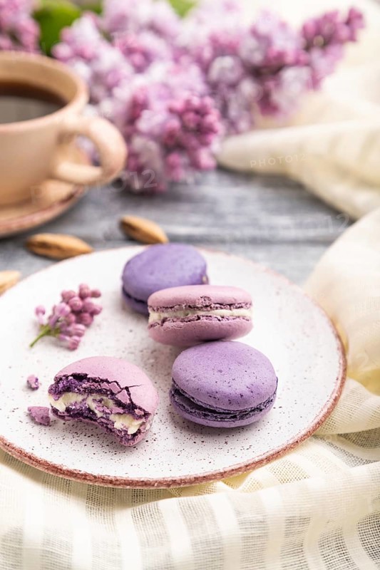 Purple macarons or macaroons cakes with cup of coffee on a gray wooden background and white linen textile. Side view, close up, selective focus