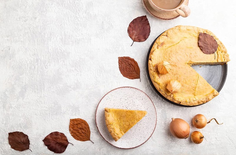 Autumn onion pie decorated with leaves and cup of coffee on gray concrete background. Top view, flat lay, copy space