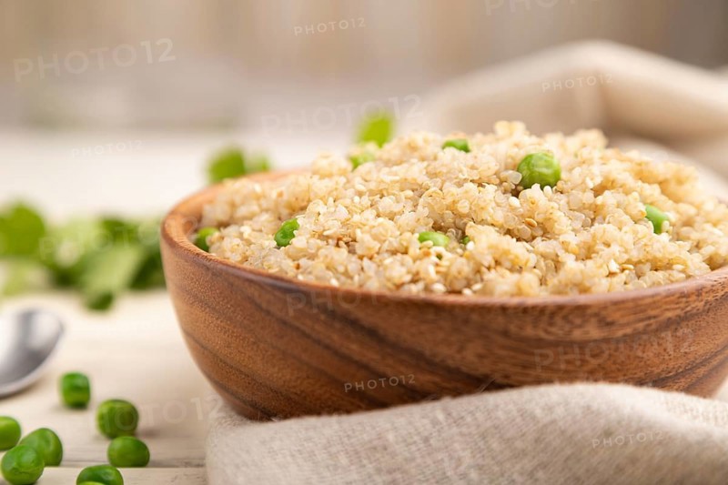 Quinoa porridge with green pea in wooden bowl on a white wooden background and linen textile. Side view, close up, selective focus