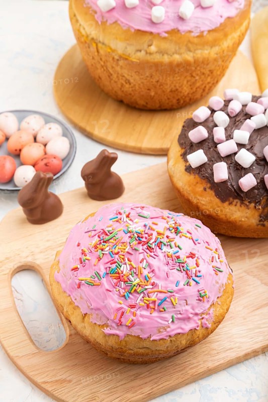 Homemade glazed and decorated easter pies with chocolate eggs and rabbits on a white concrete background and yellow textile. Side view, close up