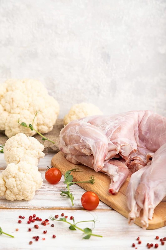 Whole raw rabbit with cauliflower, tomatoes and spices on a white wooden background and linen textile. Side view, copy space
