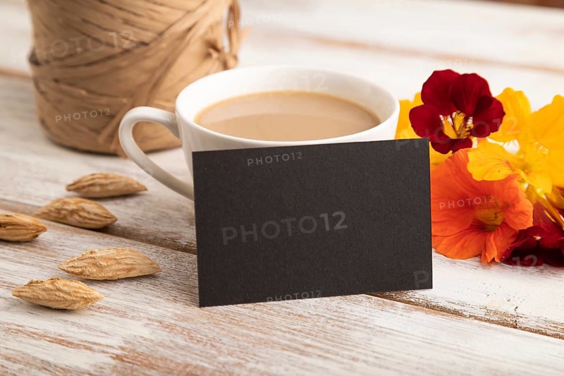 Black paper business card mockup with orange nasturtium flower and cup of coffee on white wooden background. Blank, side view, copy space, still life. spring concept