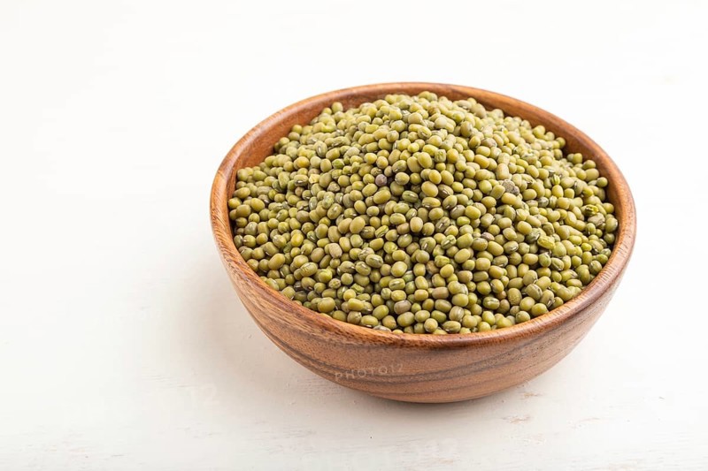 Wooden bowl with raw green mung bean on a white wooden background. Side view, close up