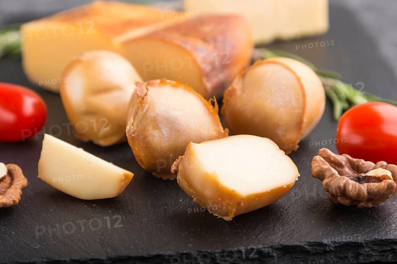 Smoked cheese and various types of cheese with rosemary and tomatoes on black slate board on a black concrete background. Side view, close up, selective focus