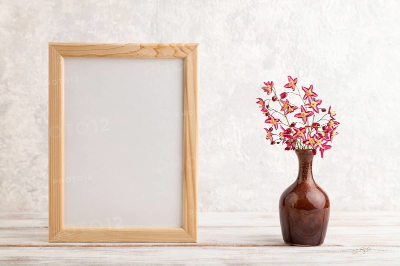 Wooden frame with purple barrenwort flowers in ceramic vase on gray concrete background. side view, copy space, still life, mockup, template, spring, summer minimalism concept