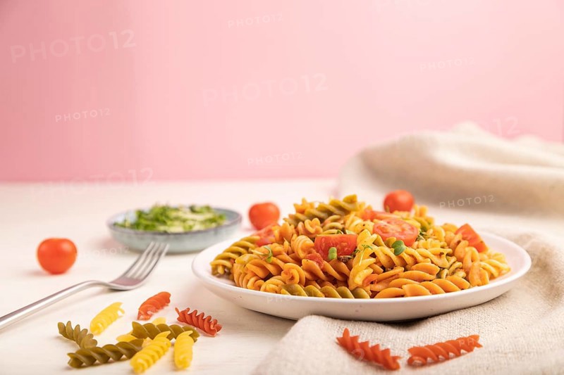 Tortiglioni semolina pasta with tomato and microgreen sprouts on a white and pink background and linen textile. Side view, copy space, selective focus