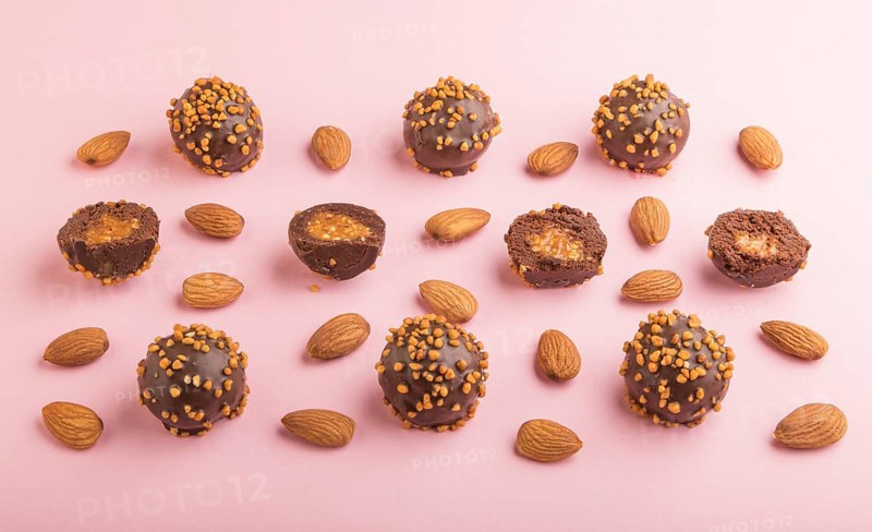 Chocolate caramel ball candies with almonds in a row on a pastel pink background. side view, close up