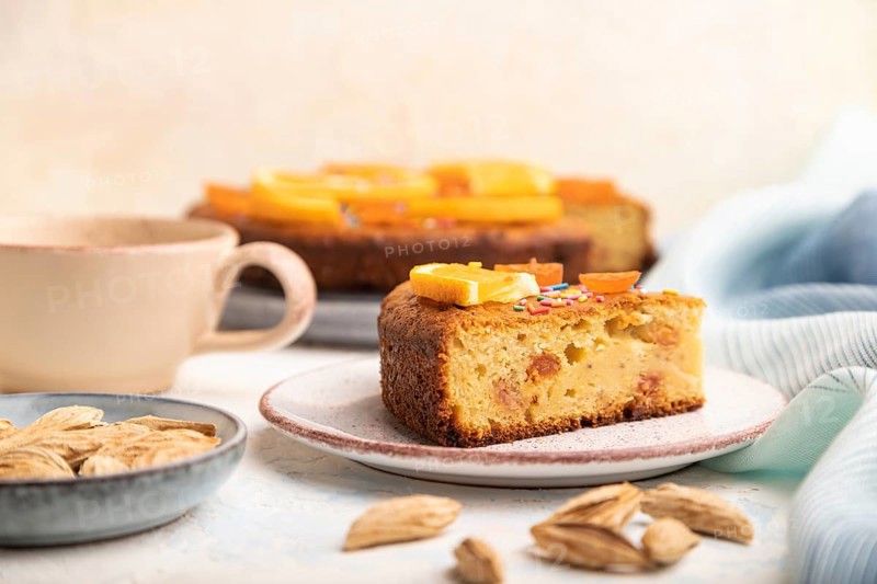 Orange cake with almonds and a cup of coffee on a white concrete background and blue linen textile. Top view, close up, selective focus