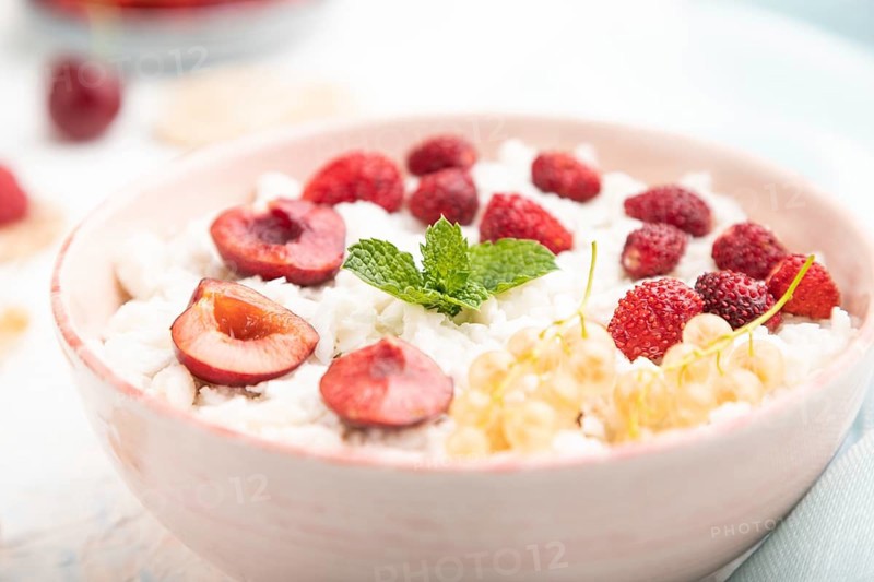 Rice flakes porridge with milk and strawberry in ceramic bowl on white concrete background and blue linen textile. Side view, close up, selective focus