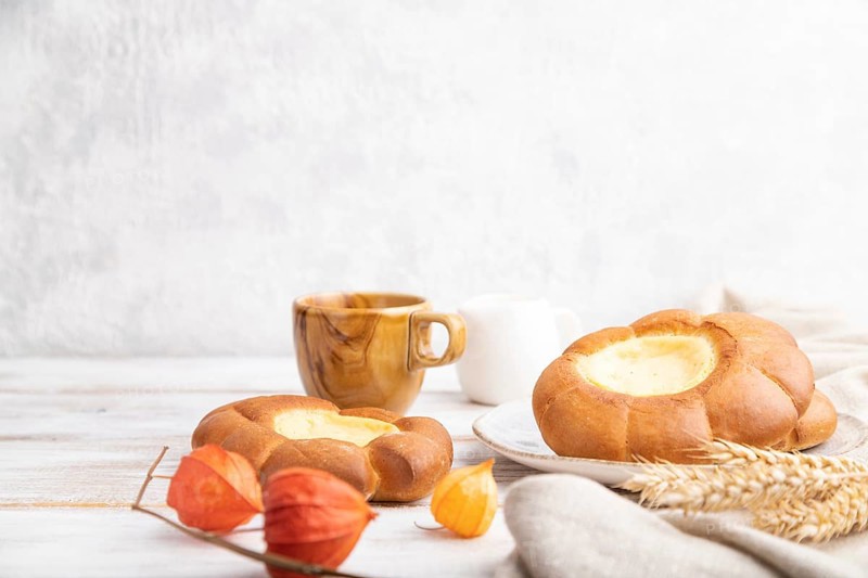 Sour cream bun with cup of coffee on a white wooden and concrete background and linen textile. Side view, close up, selective focus, copy space