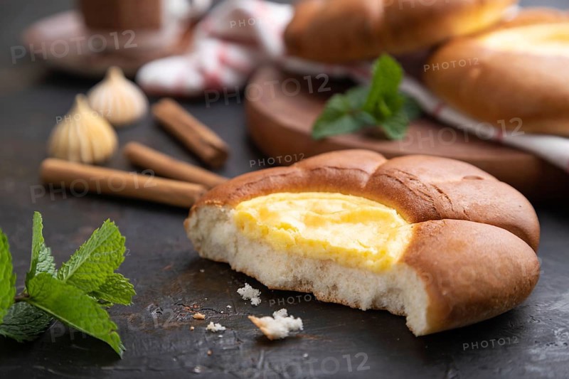 Sour cream bun with cup of coffee on a black concrete background and linen textile. Side view, close up, selective focus