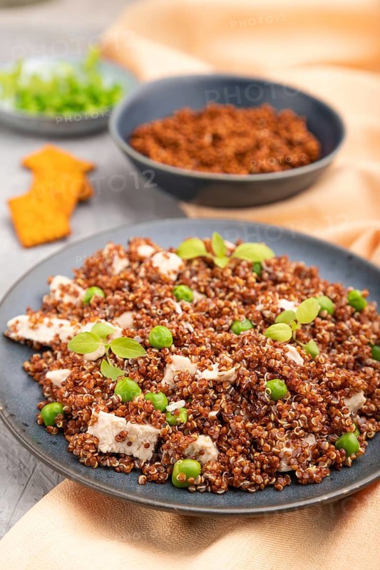Quinoa porridge with green pea and chicken on ceramic plate on a gray concrete background and orange textile. Side view, close up, selective focus