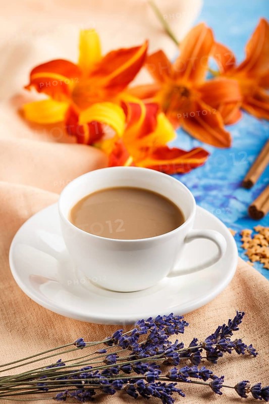 Orange day-lily and lavender flowers and a cup of coffee on a blue concrete background, with orange textile. Morninig, spring, fashion composition. side view, selective focus