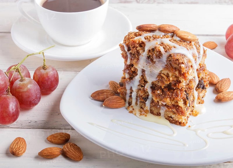 Pie with caramel, white milk sauce and almonds on a white plate on a white wooden background. close up