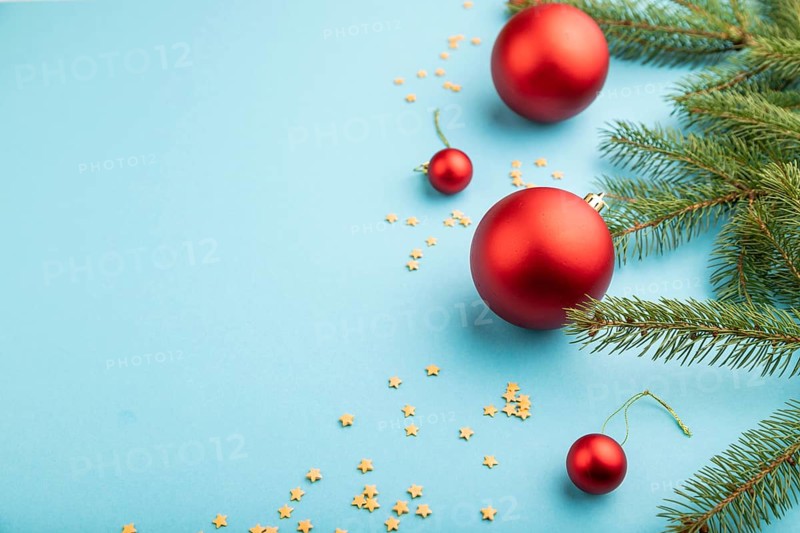 Christmas or New Year composition. Decorations, red balls, fir and spruce branches, on a blue paper background. Side view, copy space