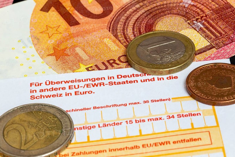Symbolic image of payment transactions: close-up of a transfer form with euro coins and euro notes