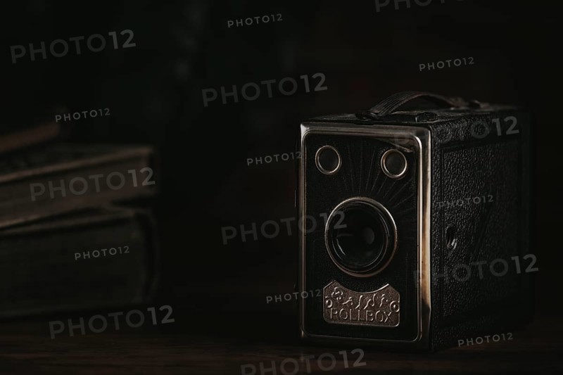 Old box camera against a dark background next to old books