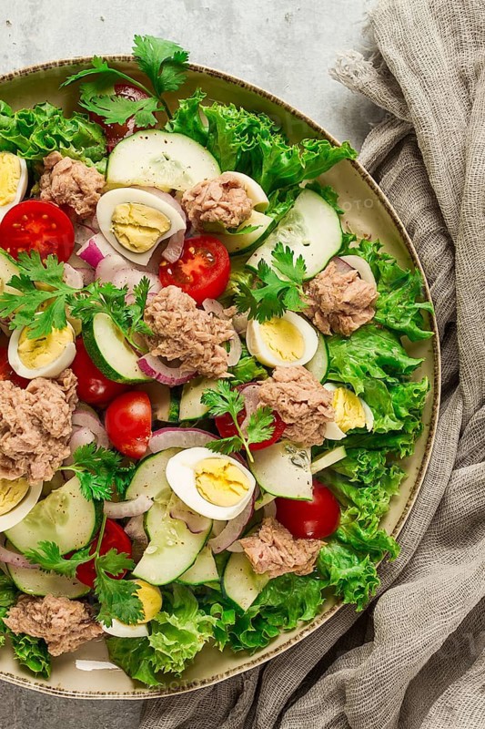 Tuna salad, vegetable salad with quail eggs, lettuce, red onion and cucumbers, on a light gray table, keto food, lifestyle, healthy eating, selective focus, top view, no people