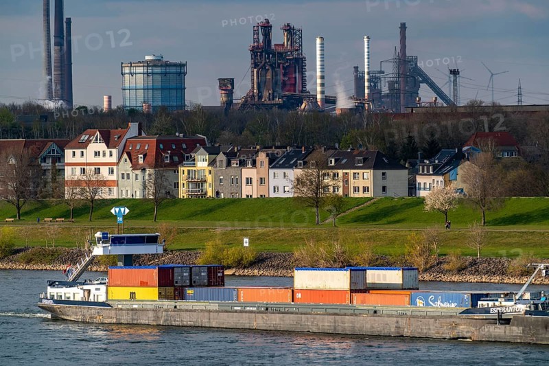 Cargo ships on the Rhine near Duisburg-Laar, houses on Deichstrasse, industrial backdrop of the ThyssenKrupp Steel steelworks in Bruckhausen, North Rhine-Westphalia, Germany, Europe