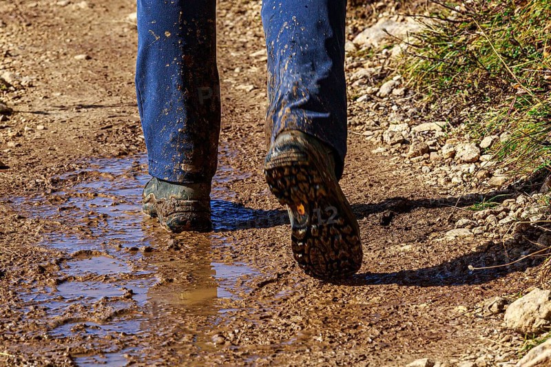 A person in hiking boots on a muddy path outdoors