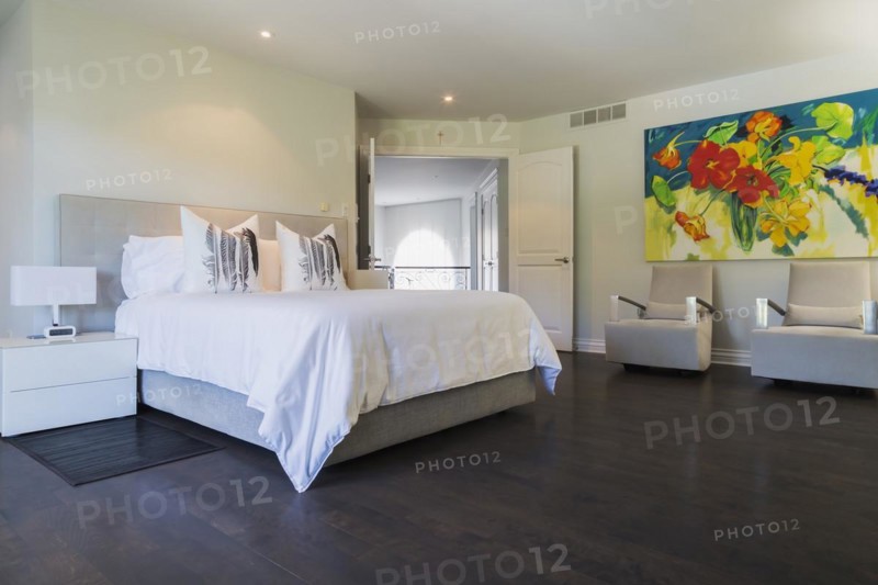 Master bedroom with queen size bed, white lacquered nightstands, upholstered armchairs and dark wooden flooring on upstairs floor inside a luxurious residential home, Quebec, Canada, North America
