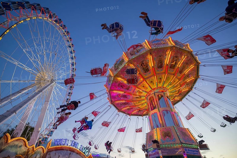 A funfair at dusk with illuminated chain carousel and Ferris wheel, Europa Rad, rides, wave flight, Cannstatter Wasen, folk festival, Bad Cannstatt, Stuttgart, Baden-Württemberg, Germany, Europe