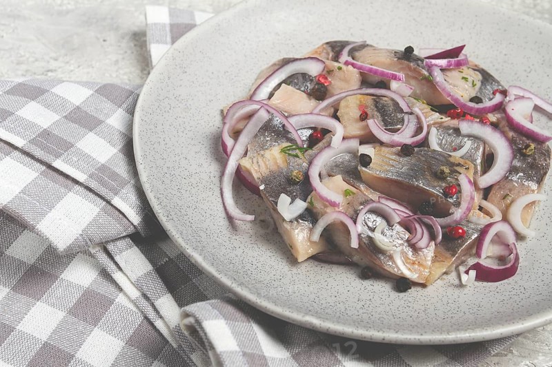 Salted herring, with spices and red onion, sliced fillet, on a plate, top view