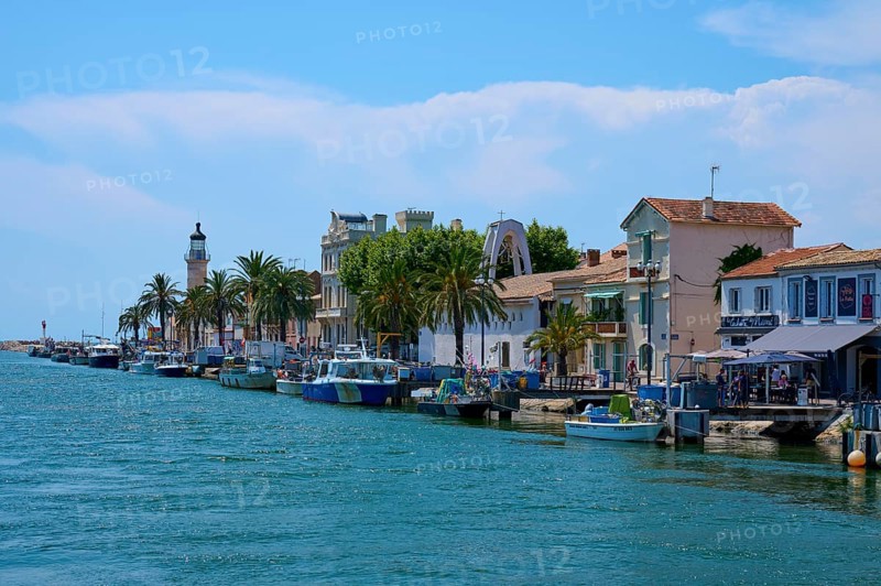Coastal town with colourful houses, boats in the water and a lighthouse in the background on a sunny day, summer, Le Grau-du-Roi, Gard, Mediterranean Sea, France, Europe