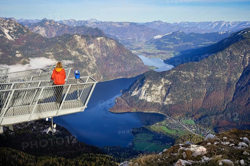 A hiker stands on the 5fingers viewpoint. View from the Dachstein Krippenstein to Lake Hallstatt. Hallstatt on the left, Obertraun on the right. Autumn, good weather. Some clouds in the mountains. Lake Hallstatt, Salzkammergut, Upper Austria, Austria, Europe