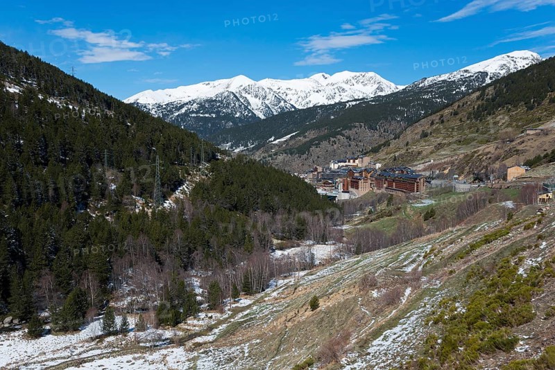 Winterliche Szenerie in einem Tal mit schneebedeckten Bergen, Gebäuden und dichten Wäldern unter einem blauen Himmel, Soldeu, Canillo, Pyrénées-Orientales, Fürstentum Andorra, Pyrenäen