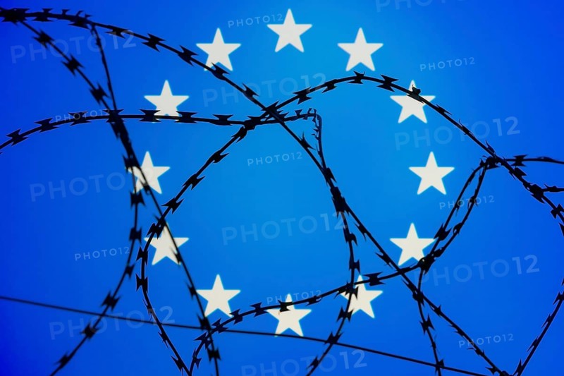 Symbolic image, migration, defence against refugees wanting to enter the EU, barbed wire overarches the stars of the EU flag against a blue sky, border, border fence
