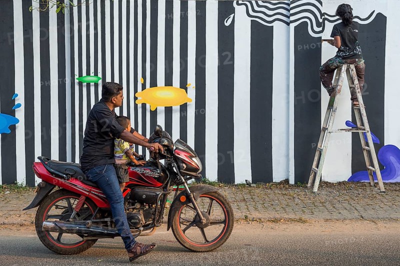 Father and son on motorbike watching Indian artist painting a wall during the International Contemporary Art Exhibition Kochi-Muziris Biennale, Fort Cochin, Kochi, Kerala, South India, India, Asia